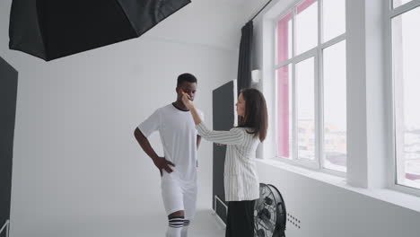 Behind-the-scenes-of-a-photo-shoot:-A-beautiful-black-model-football-player-is-preparing-for-a-photo-shoot-for-a-magazine-a-makeup-artist-corrects-the-tone-of-the-skin-for-photos-in-a-sports-magazine